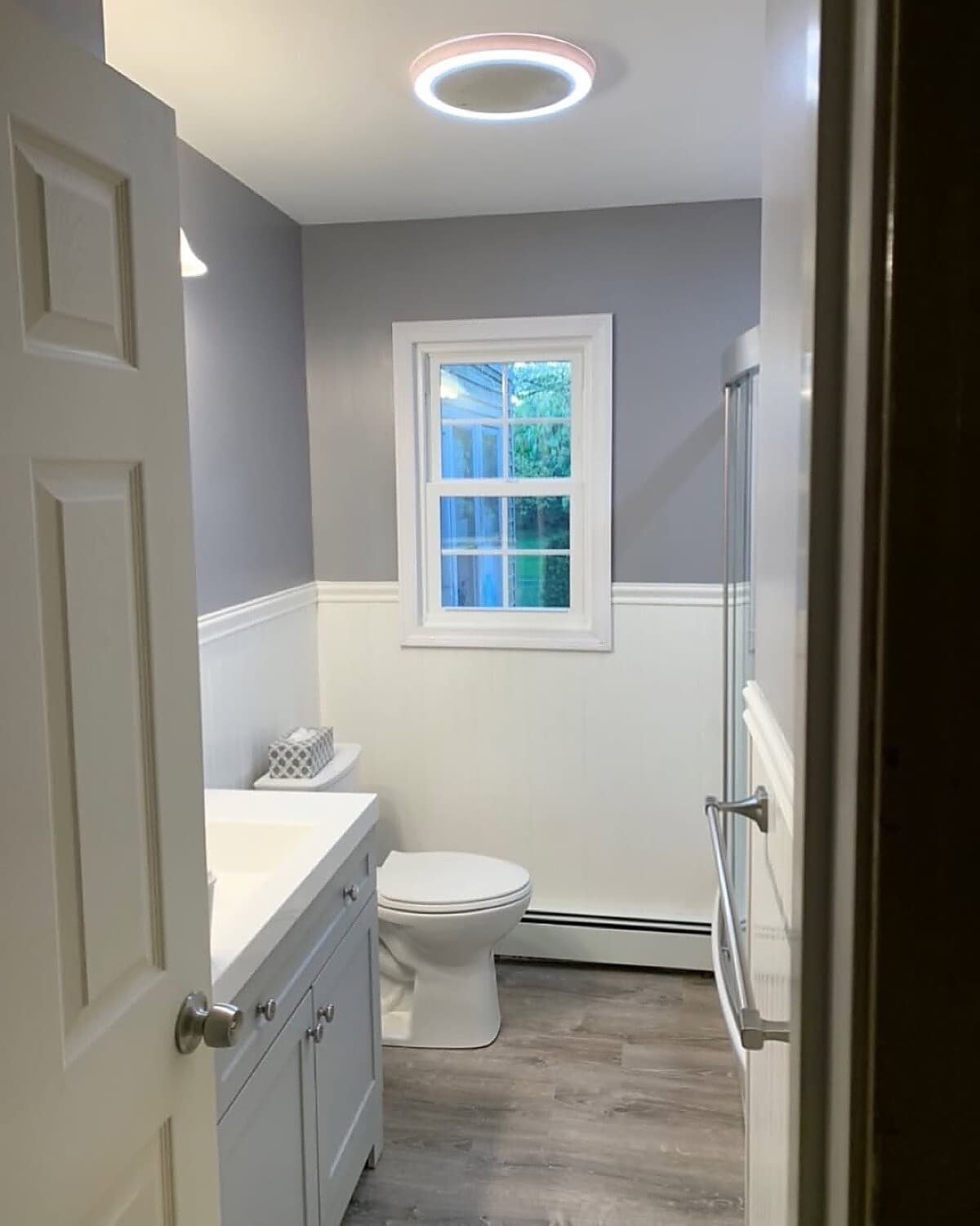 Bathroom with blue-gray wainscoting, white vanity, and glass shower