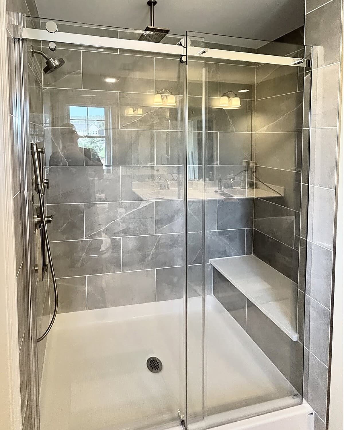 Gray stone tile shower with built-in bench and frameless glass door